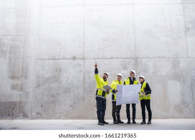 A Group Of Engineers Standing Against Concrete Wall On Construction Site.