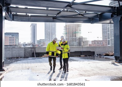 Group Of Engineers Standing Outdoors On Construction Site, Using Tablet.