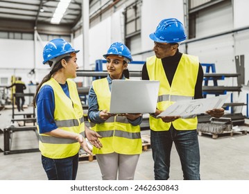 Group of engineers wearing safety gear discussing plans in an industrial warehouse, using a laptop. - Powered by Shutterstock