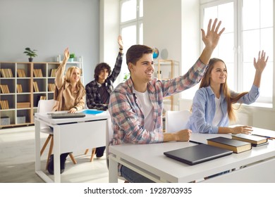 Group Of Enthusiastic Male And Female High School Or College Students Sitting At Desks And Raising Hands In Class. Pupils Voting, Willing To Answer Question Or Eager To Take Part In Classroom Activity