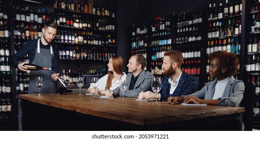 Group Of European Friends And African Woman At Wine Tasting Master Class In Restaurant, Sommelier Pours Drink Into Decanter.