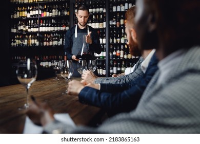 Group Of European Friends And African Woman At Wine Tasting Master Class In Restaurant, Sommelier Pours Drink Into Decanter.