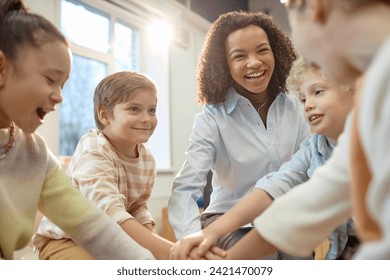 Group of excited children huddling for motivation in school with smiling female teacher enjoying work - Powered by Shutterstock