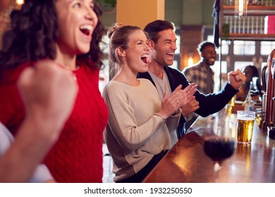 Group Of Excited Customers In Sports Bar Watching Sporting Event On Television