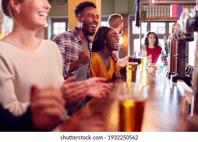 Group Of Excited Customers In Sports Bar Watching Sporting Event On Television