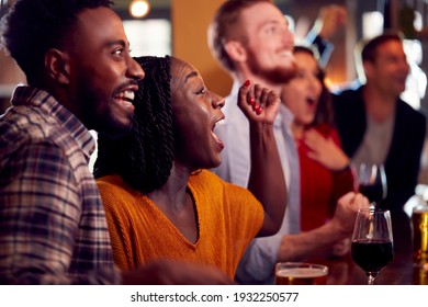 Group Of Excited Customers In Sports Bar Watching Sporting Event On Television