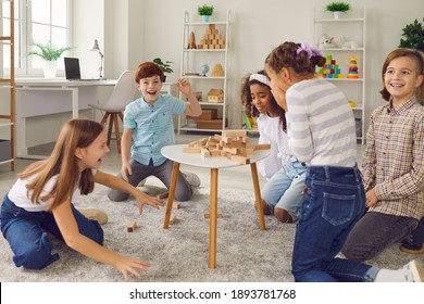 Group Of Excited Diverse 8-10 Year Old Children Laughing At Broken Wood Block Tower While Playing Stacking Board Game Together At Home Or In After School Kids Club. Fun Party Activities Concept