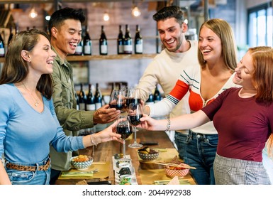 Group Of Excited Happy Young Friends Sharing A Toast Together As They Clink Their Glasses Of Red Wine While Enjoying A Meal In A Pub Or Restaurant Celebrating A Special Occasion