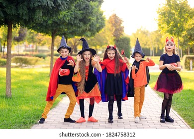 Group Of Excited Kids In Costumes Smiling And Running On The Lawn Celebrating Halloween In The Park