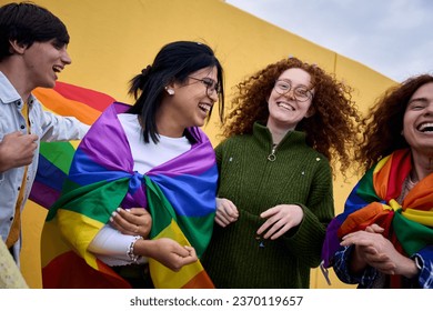 Group excited young diverse people laughing yellow wall background. LGBT community enjoying gay pride day outdoors. Liberal people celebrating street party. Rainbow flags and friends of generation z. - Powered by Shutterstock