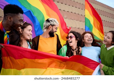 Group of excited young friends enjoying together on gay pride day. Joyful people gathered from LGBT community hugging laughing outdoors. Generation z and open minded. 