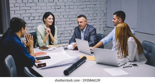 Group Of Executive Managers In Formal Clothing Sitting At Desktop With Modern Netbooks And Talking About Designed Sketch, Professional Architects Collaborating On Blueprint During Working Process