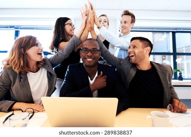 Group Of Executives Smiling And Group High Fiving Over Black Colleague's Head