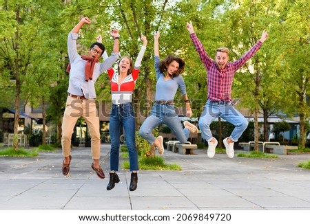 Group of exuberant young friends cheering and leaping in the air with arms raised in celebration outdoors in a park