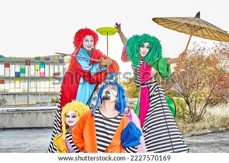 Group of face-painted performers in colorful clown costumes and wigs juggling and dancing on stilts during the parade in the city park.