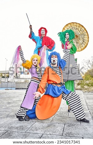 Group of face-painted performers in colorful clown costumes and wigs juggling and dancing on stilts during the parade in the city park.