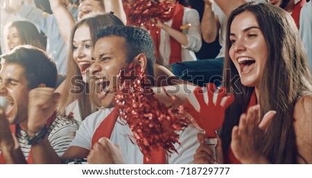 Group of fans cheer for their team victory on a stadium bleachers. They wear casual fan clothes.