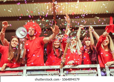 Group Of Fans Dressed In Red Color Watching A Sports Event In The Stands Of A Stadium