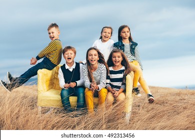Group of fashion children wearing same style clothing playing on a sofa in the autumn field. Fall casual outfit in navy and yellow colors. 7-8, 8-9, 9-10 years old models sitting on a coach outdoor.