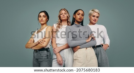 Group of fashionable women standing together in a studio. Diverse women looking at the camera while standing against a studio background. Four female friends looking confident in a studio.