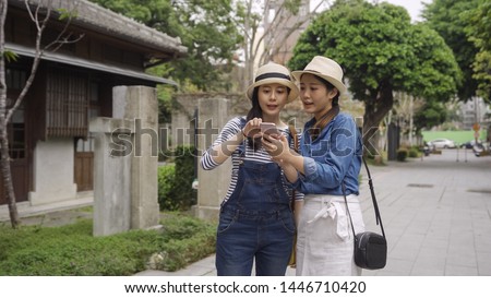 group of female asian travelers holding smartphone point touching screen standing in outdoor street in kyoto japan old town. elegant young girls talking discussing direction of tourist attraction.