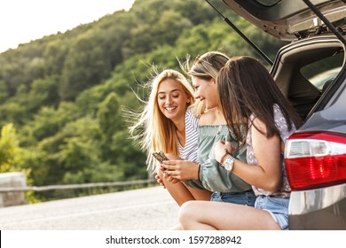 Group Of Female Best Friends On Travel . They Sitting On Car Trunk And Relaxing After Long Journey.	
