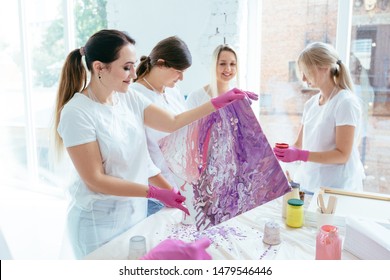 Group of female creating and slowly whirling canvas with liquid acrylics abstract painting in art therapy class. Teamwork, study, art therapy concept.