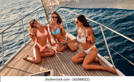 Group of female friends relaxing on luxury yacht. Three beautiful girls in swimsuits sitting on yacht deck,drinking beer and having fun together while sailing in the sea.Traveling and yachting concept