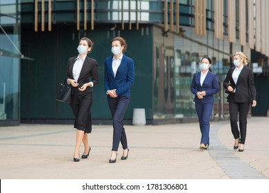 Group Of Female Managers In Office Suits And Masks, Walking Together Past City Building, Talking, Discussing Projects. Full Length Business During Covid Epidemic Concept