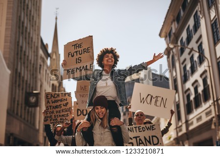 Group of female protesters marching on the road with signboards and smiling. Women holding protest banners and marching outdoors.