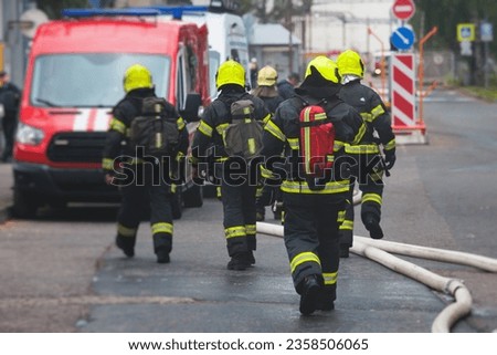 Group of fire men in protective uniform during fire fighting operation in the city streets, firefighters brigade with the fire engine truck vehicle in the background, emergency and rescue service