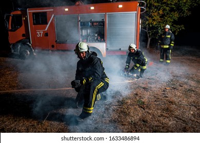 Group Of Firemen Putting Out A Fire With A Long Water Hose