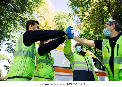 Group of first aid personnel with ambulance high-five with their hands as a sign of success after an emergency call during the Coronavirus pandemic, Covid-19 - Concept of teamwork and union - Powered by Shutterstock