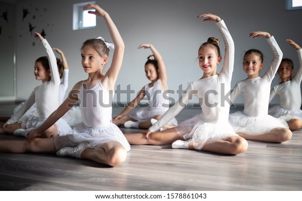 Group of fit happy children exercising ballet in\
studio together
