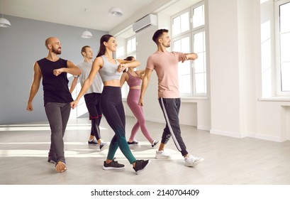 Group Of Fit Young People Doing Physical Exercises With A Fitness Instructor At The Gym. Team Of Happy Men And Women Enjoying An Aerobics Or Sports Dance Workout Class With A Professional Teacher