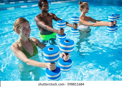 Group of  fit young people doing aqua fitness exercise with plastic dumbbells in swimming pool on summer sunny day outdoors
