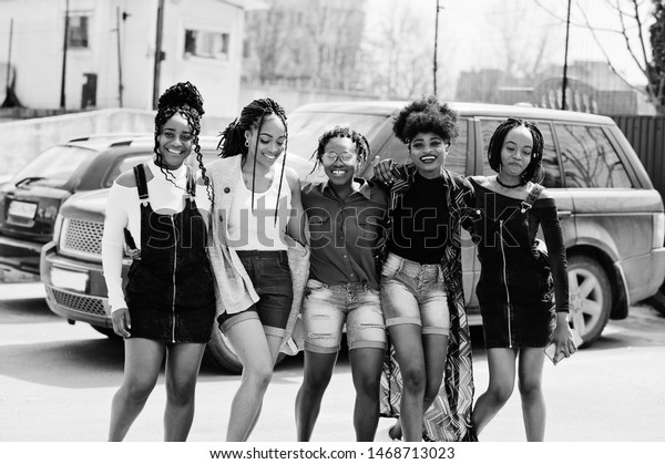Group of five african american woman\
walking on road together against suv car on\
parking.