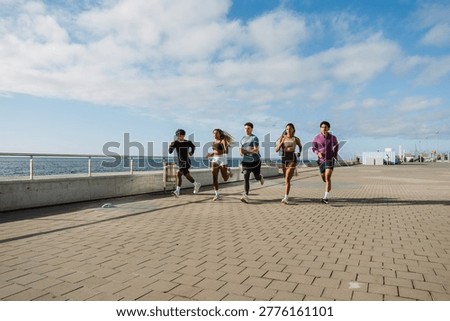 A group of five athletes running side by side and looking ahead near the sea