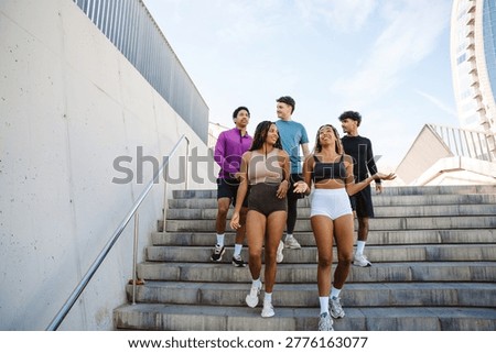 A group of five athletes walk down the stairs and talk while smiling