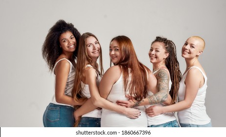 Group Of Five Beautiful Diverse Young Women Wearing White Shirt Putting Arms Around Each Other, Looking At Camera While Posing Together Isolated Over Grey Background. Diversity, Body Positivity.