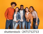 Group of five diverse young adults standing in front of a yellow background. They are all smiling and looking at the camera. The group appears to be friends and is enjoying each others company.