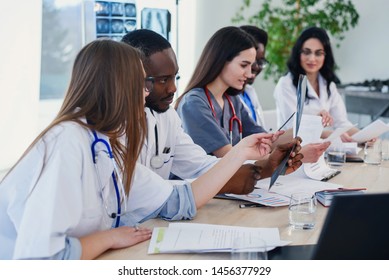 Group of five doctors are studying disease patient's history. Team of multiethnic young doctors having a meeting in conference room in the modern bright hospital.