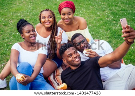 group of five friends female and male taking selfie on camera smartphone and having fun outdoors lifestyle near lake,eating burger picnic in the park
