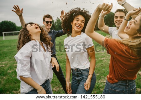 Group of five friends having fun at the park - Millennials dancing in a meadow among confetti thrown in the air - Day of freedom and carefree