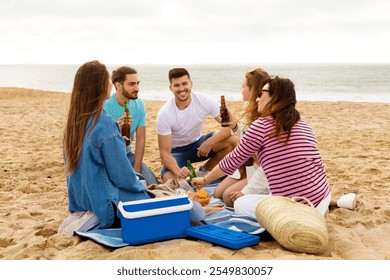 A group of five friends relaxes on the sandy beach, sharing snacks and drinks. They laugh and chat, enjoying each other's company against the backdrop of the ocean waves. - Powered by Shutterstock