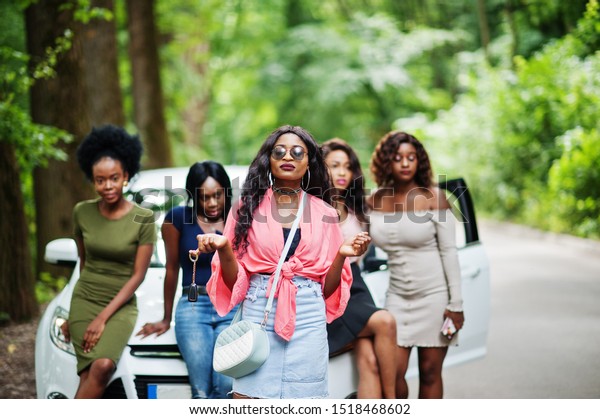Group of five happy african american girls\
posed against car, one of them show\
keys.