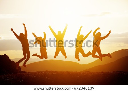 Group of five happy friends jumps at sunset time on background mountains