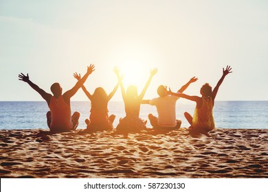 Group Of Five Happy People Sits On Background Of Empty Sunset Beach. Travel Or Sea Vacations Concept