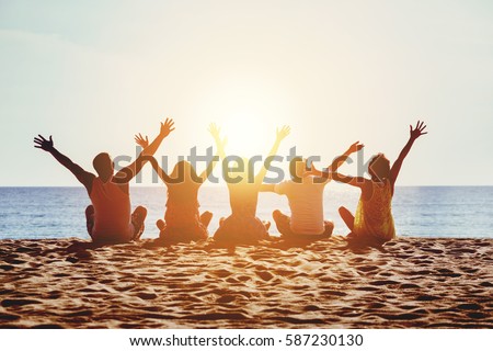 Group of five happy people sits on background of empty sunset beach. Travel or sea vacations concept
