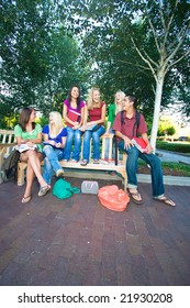 Group Of Five Laughing High School Girls And One Boy Sitting On A Bench Holding Books. Vertically Framed Photo.